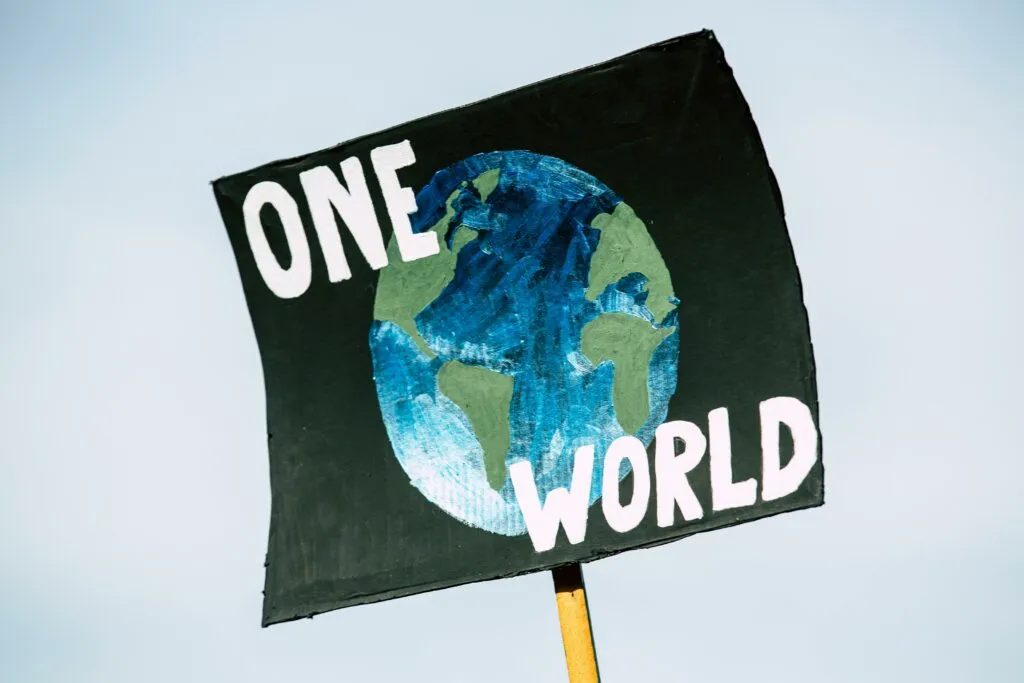Panneau tenu à bout de bras affichant la Terre et le texte « One World ».